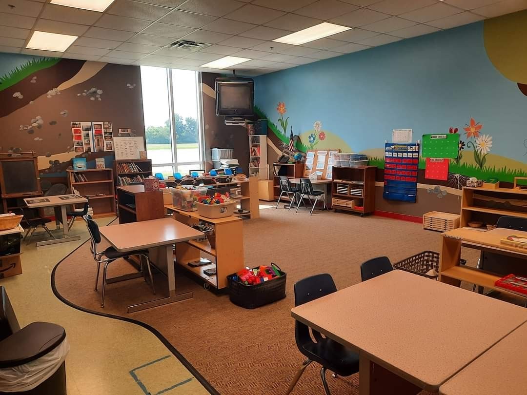 Another view of the classroom, with more tables, shelves, and a window.